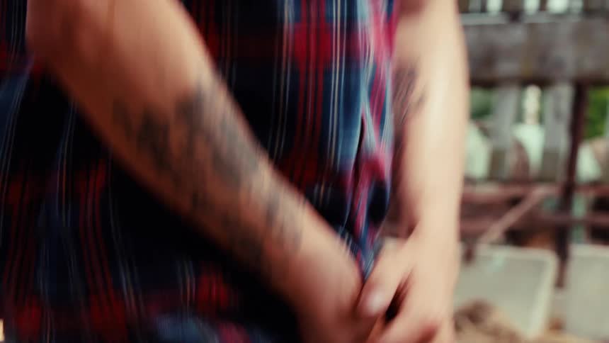 A close-up shot of a man's hands and his 'Peace of Mind' tattoo as he stands pensively in a rural setting before walking away into a blur