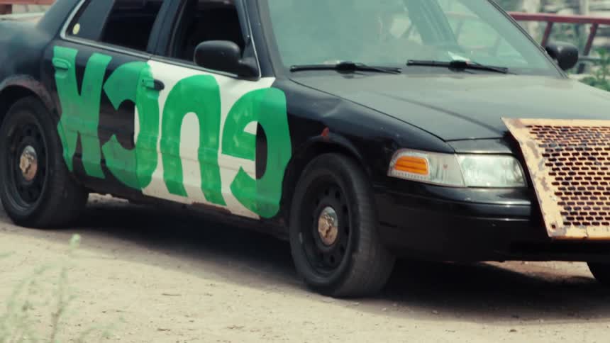 A rugged, customized demolition derby car with 'KONG' spray-painted on the side sits in a junkyard