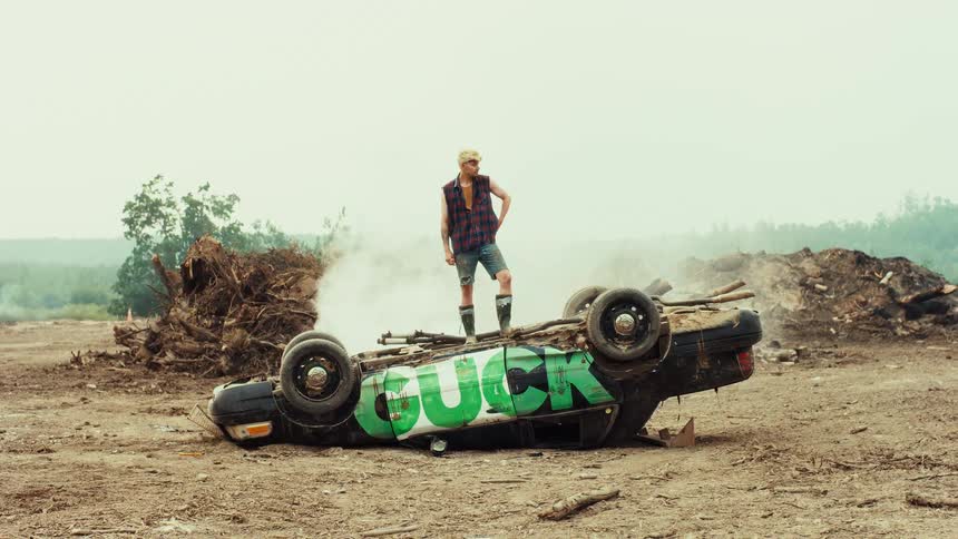 A defiant punk stands atop an overturned car spray-painted with graffiti in a smoky, desolate landscape
