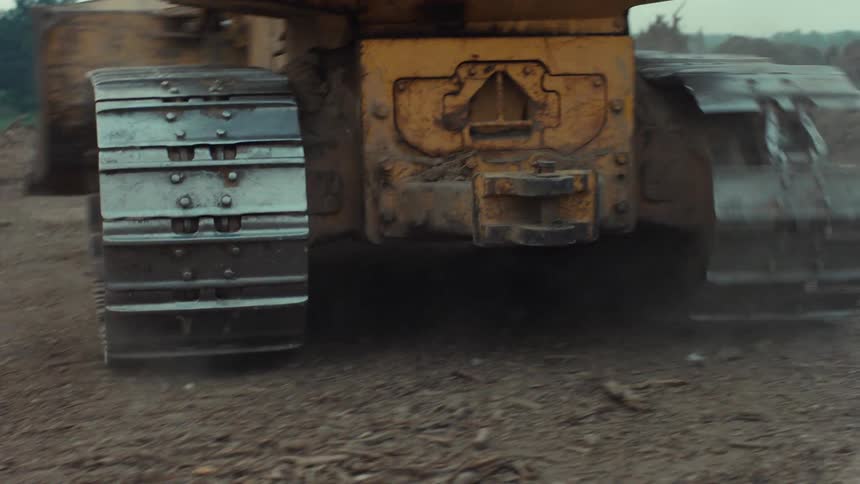 A close-up of a John Deere bulldozer's metal treads turning as it reverses on a dirt construction site
