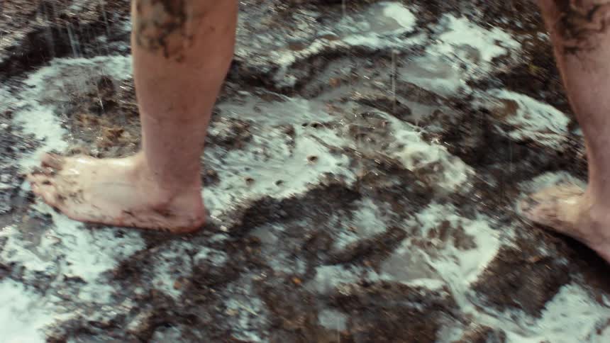 Close up slow motion shot of a person's muddy feet and legs being rinsed off in a puddle of soapy water
