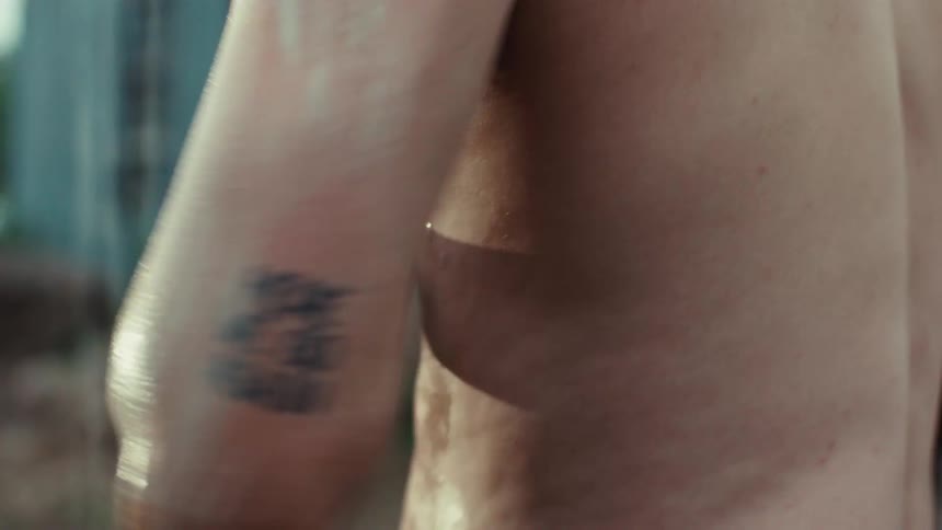 A close-up, slow-motion shot of a tattooed man lathering up with soap while taking a shower