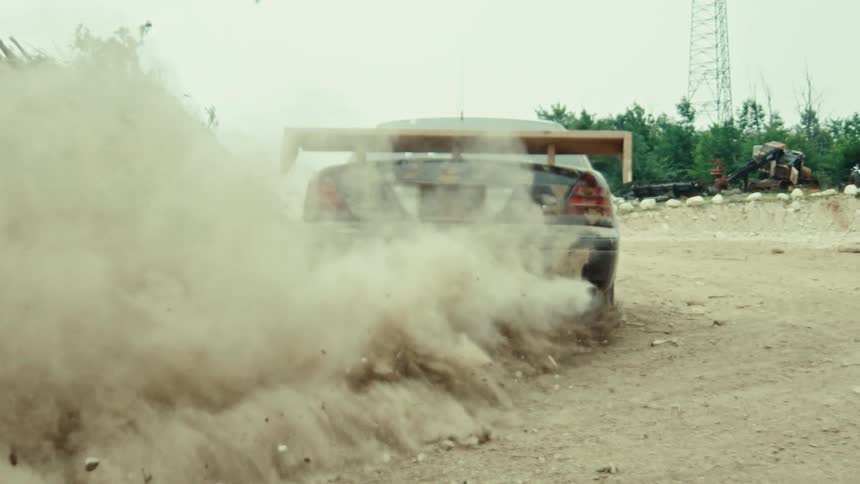 A modified race car does a powerful burnout on a dirt road, kicking up a massive cloud of dust in super slow motion