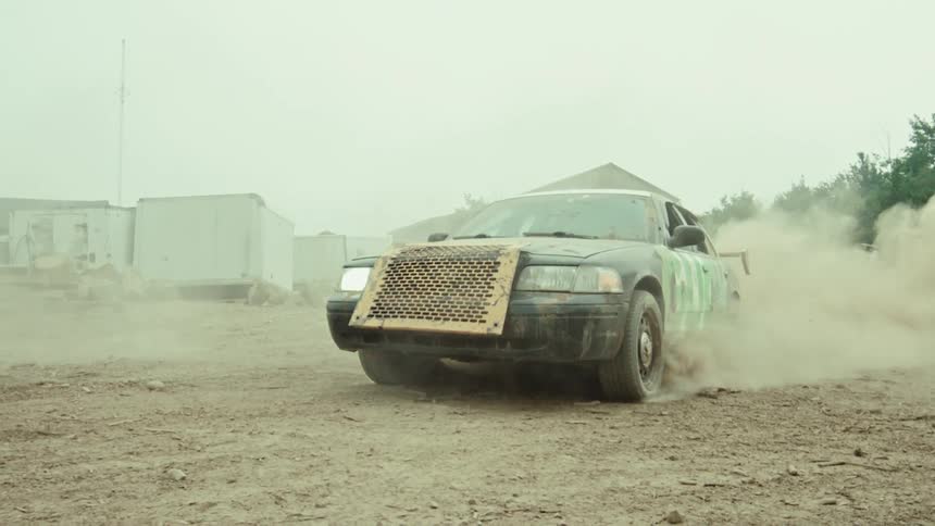 A modified race car does a burnout in slow motion, kicking up a large cloud of dirt and dust in an industrial lot