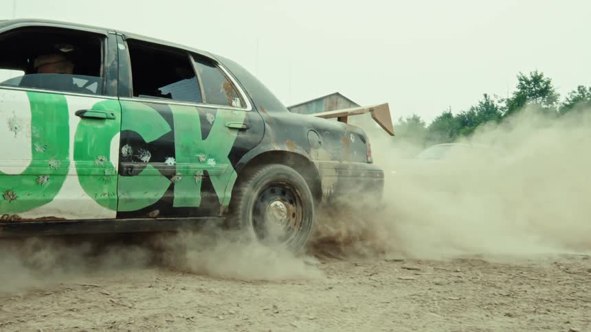 A custom race car with provocative graffiti does a powerful burnout in a dusty lot, creating a massive cloud of dirt in slow motion