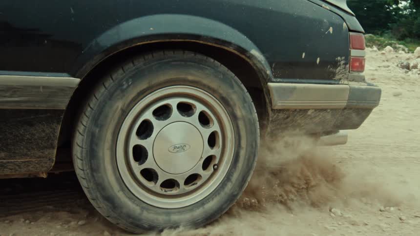 Close-up of a vintage car's wheel spinning in slow motion, kicking up a cloud of dust from a dirt road