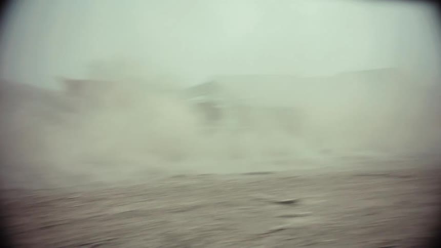 Gritty slow-motion footage of two cars in a post-apocalyptic style paintball battle, kicking up dust in a desolate yard