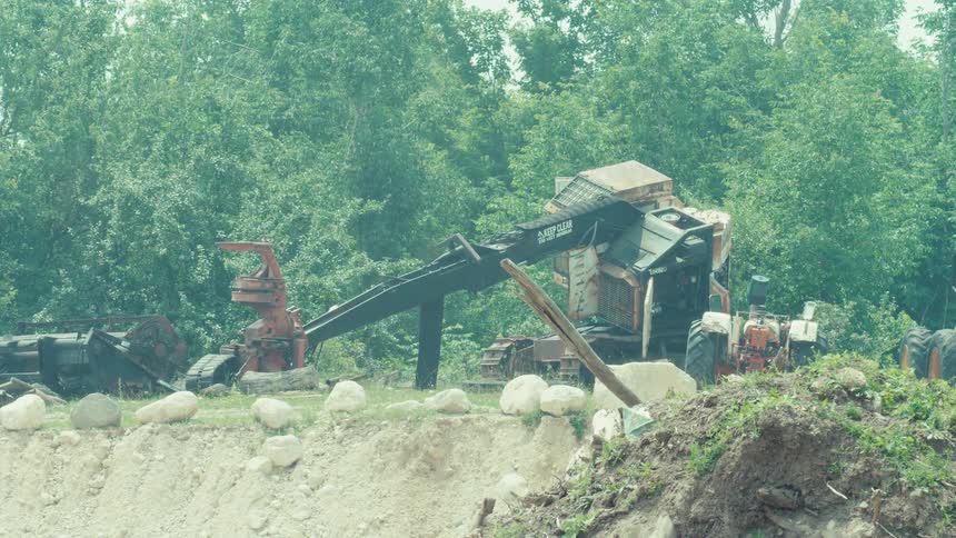 Old, rusted heavy machinery sits abandoned in a rural scrapyard on a hot, hazy day