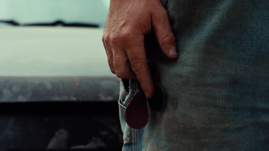 Close up of a man's weathered hand nervously fidgeting with his car keys while standing next to his truck