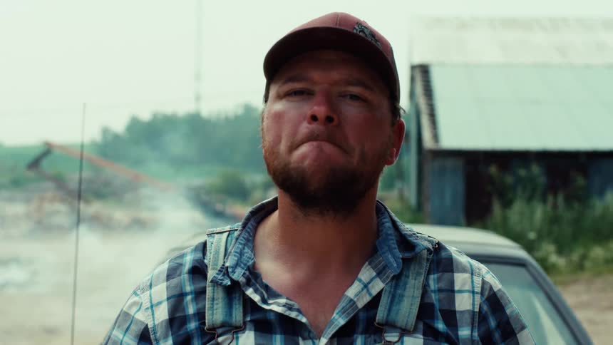 Cinematic close-up of a rugged, determined farmer looking seriously into the camera on a hazy day
