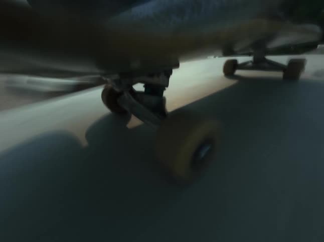 A dynamic low-angle point-of-view of a skateboard rolling to a stop in a concrete skatepark