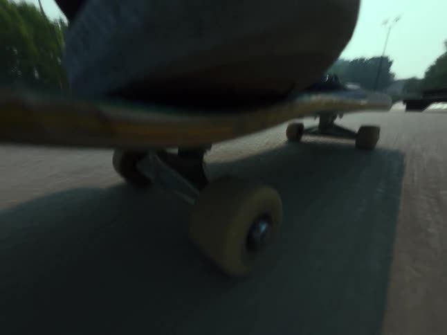 A low-angle point-of-view shot from a skateboard as it rolls across the concrete at a skatepark and performs a trick