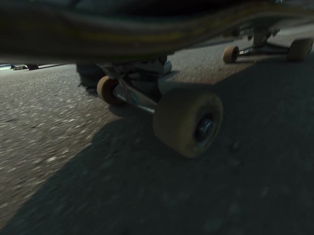 A dramatic low-angle shot from under a skateboard as it glides across pavement and comes to a stop
