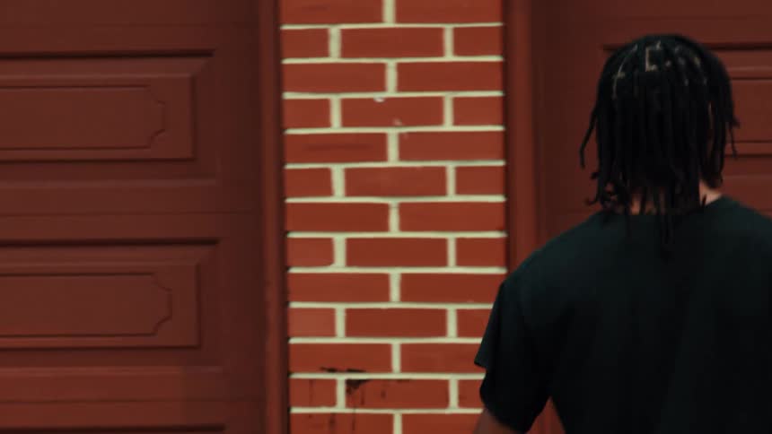 Slow motion tracking shot of a young Black man with dreadlocks walking down a gritty city alleyway past graffiti-covered walls