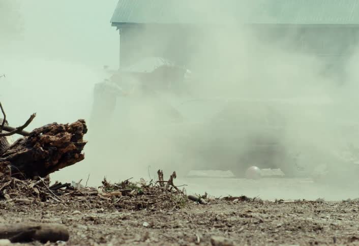 A frustrated man throws his bowling ball helmet and kicks his smoking car as a derby car speeds by kicking up dust