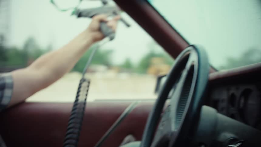 Close-up on the steering wheel of a vintage car during a chaotic paintball gun battle