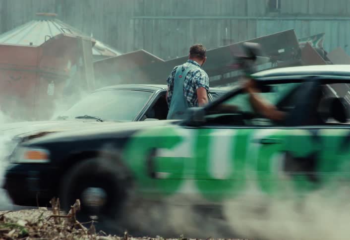 Slow motion of a demolition derby car hitting a man in overalls and speeding off into a cloud of dust