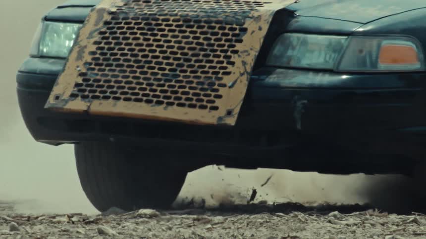 Close up slow motion shot of a rugged modified car doing a burnout in the dirt, kicking up dust as the camera pulls away
