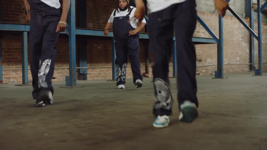 Low-angle shot of three dancers performing intricate and synchronized Pantsula footwork in an industrial warehouse