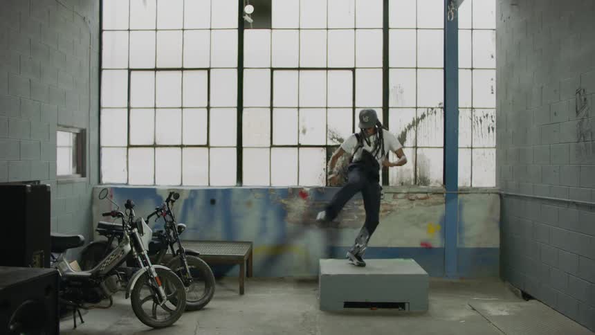 A stylish dancer performs an energetic freestyle hip-hop routine on a platform inside a gritty industrial warehouse