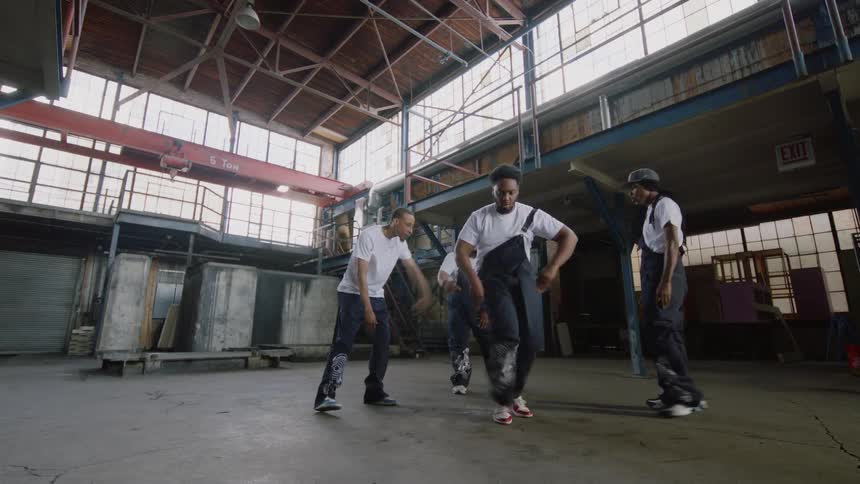 A crew of male dancers takes over an industrial warehouse, showing off their powerful and intricate street dance skills