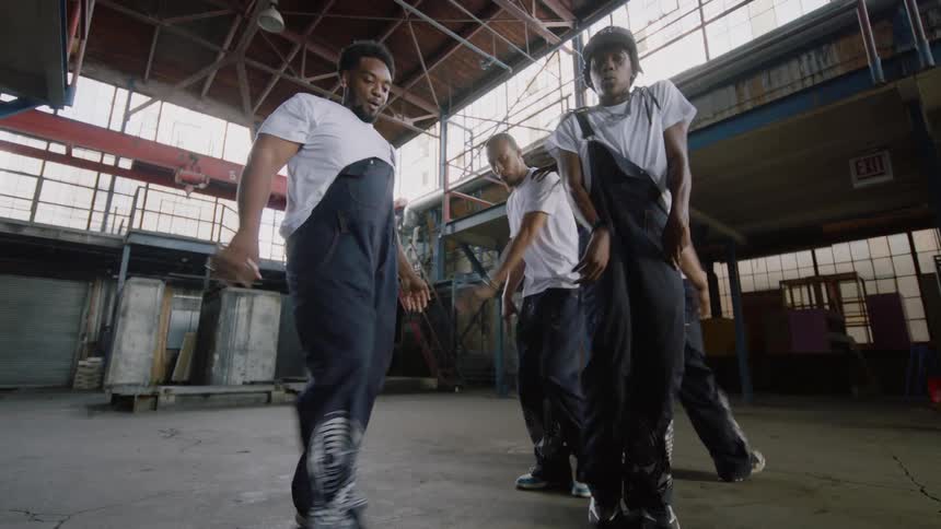 A talented group of four male dancers performs a synchronized hip-hop routine in a spacious industrial warehouse