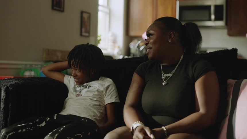 A young African American mother and her son share a happy moment, smiling and talking while relaxing together on the couch at home