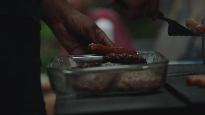 Cooking sausages on a grill and moving them to a glass dish in slow motion