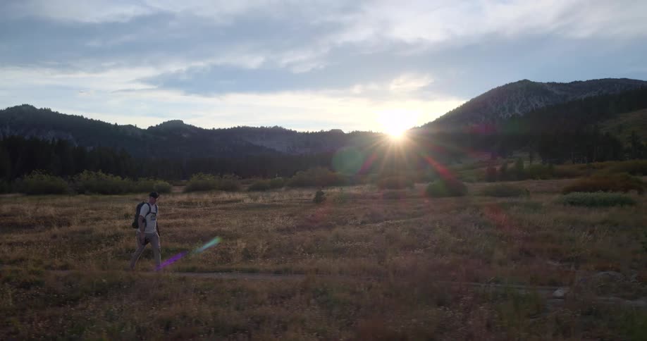 An adventurous hiker explores a beautiful mountain meadow during a stunning sunset in slow motion