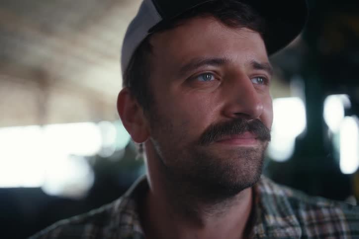Close-up cinematic portrait of a thoughtful man with a mustache and hat looking contentedly off-camera indoors