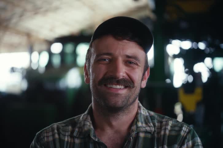 Close-up portrait of a friendly farmer with a mustache smiling while standing inside a rustic barn