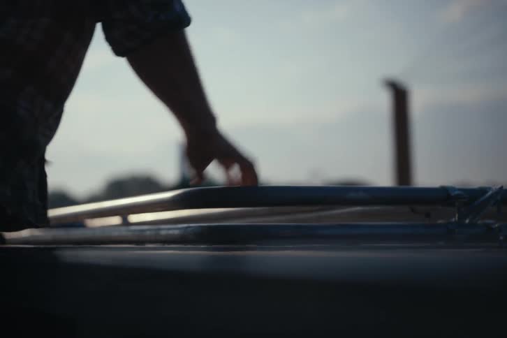 A worker in a plaid shirt carefully loads metal equipment onto the roof of a vehicle