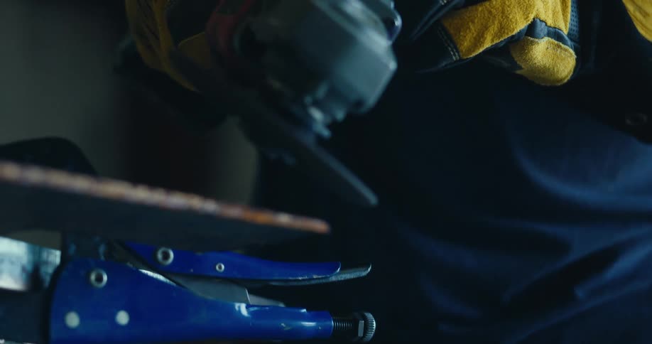 A close-up slow-motion shot of a worker grinding a metal blade, sending a cascade of bright orange sparks into the air