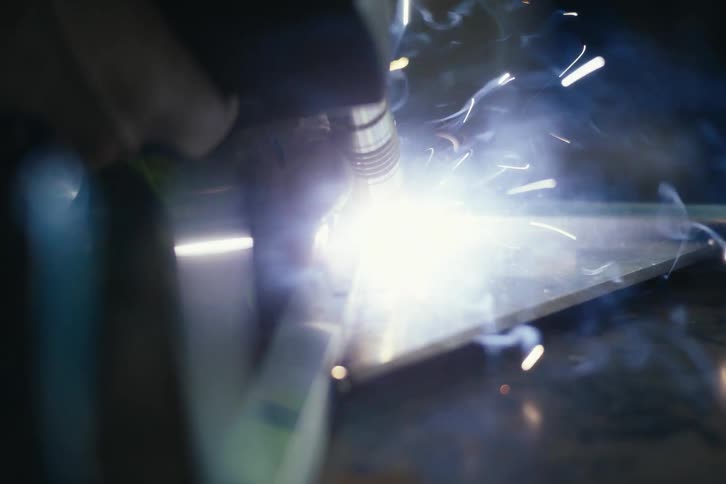 Extreme close-up of a professional welder joining two pieces of metal with a bright torch, sending sparks flying in a workshop