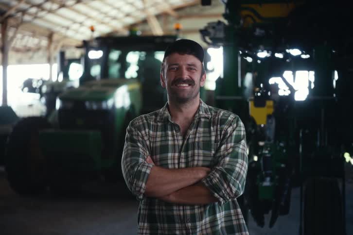 Portrait of a proud farmer standing with arms crossed in front of his tractor inside a barn