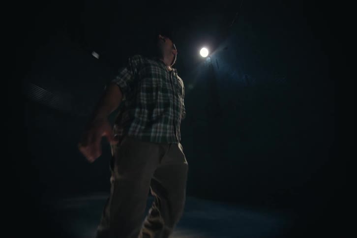 A farmer stands inside a dark grain silo, illuminated by a single spotlight as he inspects the empty structure
