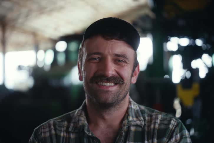 Close-up portrait of a happy male farmer with a mustache smiling in a barn