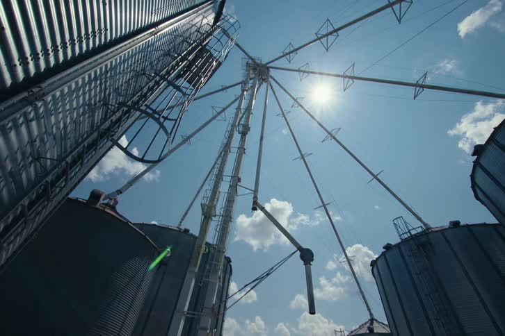 A low-angle upward tilt reveals the impressive scale of grain silos and their connecting machinery against a bright sunny sky