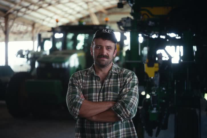 Portrait of a proud farmer with a mustache standing confidently in front of his agricultural machinery in a barn