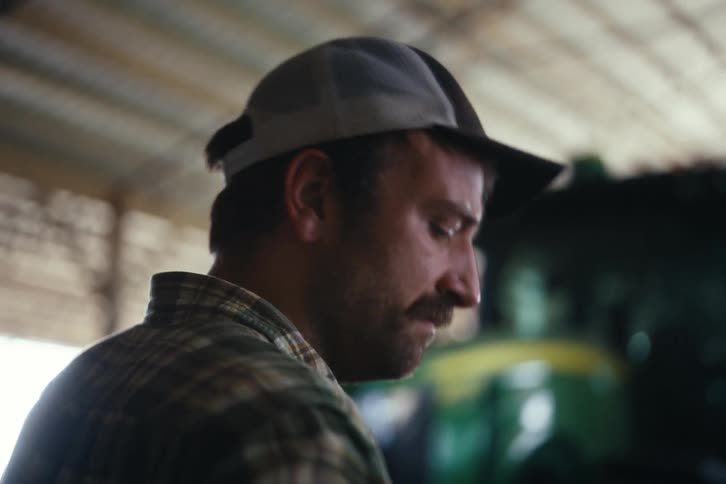 Slow motion close-up of a thoughtful farmer in a plaid shirt adjusting his cap inside a barn