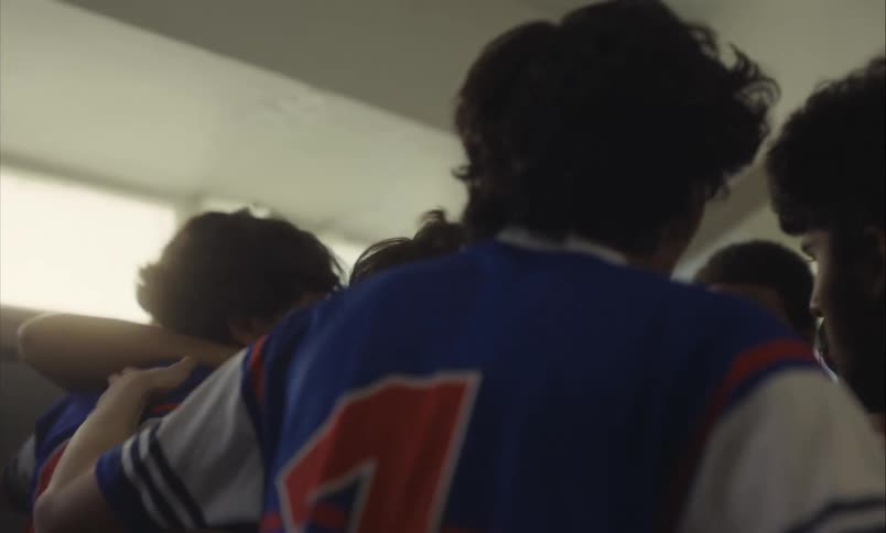A team of young men in rugby uniforms come together in a huddle while their captain gives an inspiring speech