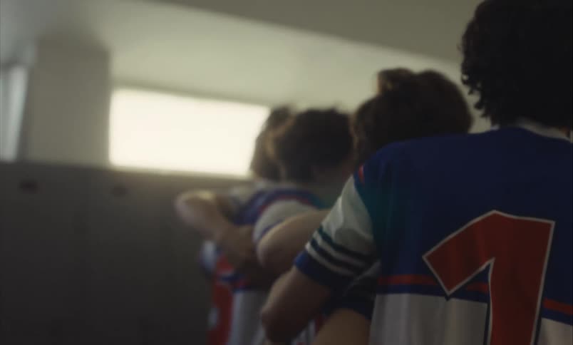 From behind, a slow motion shot of a male sports team in a group huddle in the locker room, showing unity and focus before a match