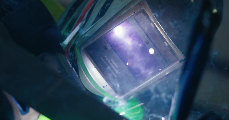 Dramatic slow-motion close-up of a welder joining metal, with brilliant sparks and smoke reflecting in the protective mask