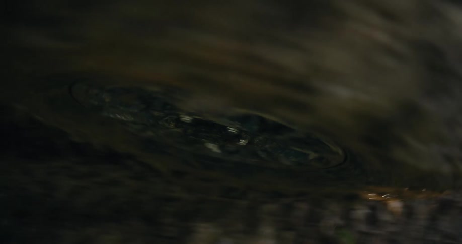 A mesmerizing macro shot of a small vortex forming in murky water, creating continuous ripples on the surface