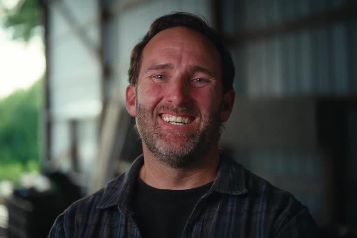 Close-up portrait of a happy, rugged man smiling warmly at the camera in his workshop or barn