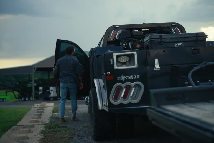A man in a plaid shirt gets out of his large black work truck with an attached trailer