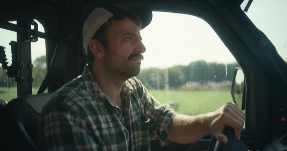 Close-up profile of a focused farmer with a mustache driving a utility vehicle across his farm on a sunny day