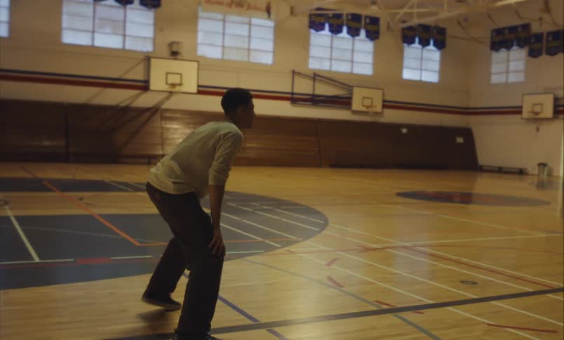 A young man throws a ball and plays defense in slow motion during a game of dodgeball in a school gymnasium