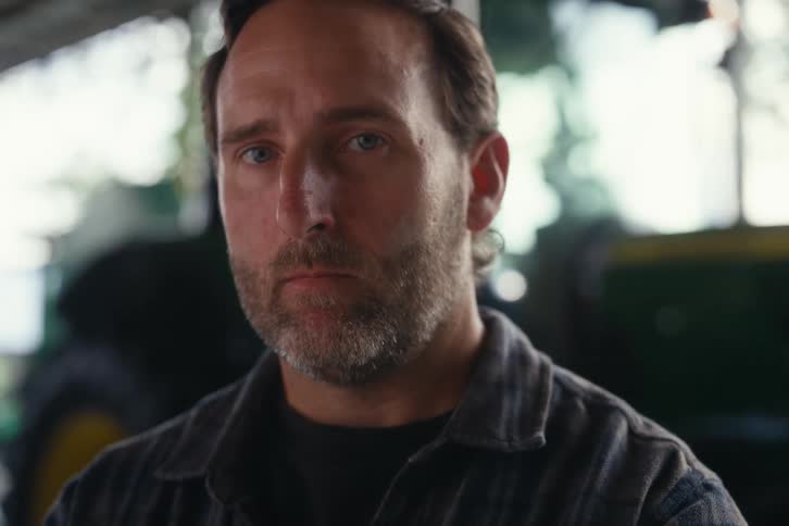 A close-up portrait of a thoughtful farmer looking up with a serious and determined expression inside a barn
