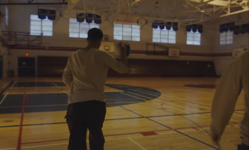 A young man practices a volleyball serve alone in an empty high school gymnasium